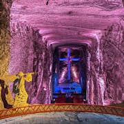 Catedral subterránea con una cruz iluminada con neón, una estatua de Jesús llevando una cruz y bancos dispuestos en un pasillo.